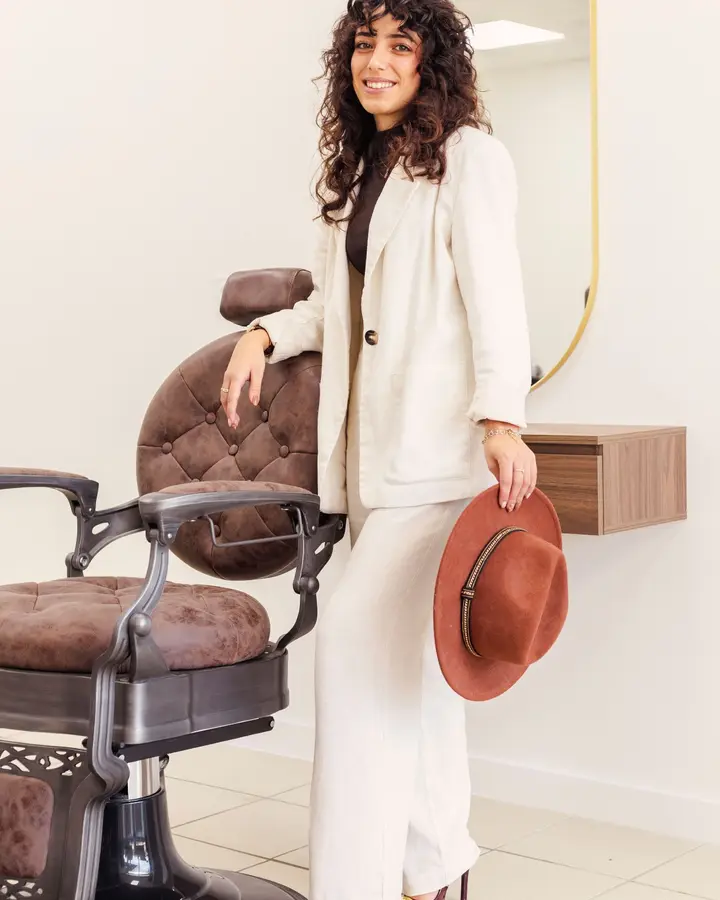 Jessica Afonso, chapeau à la main, à côté du fauteuil de barbier vintage