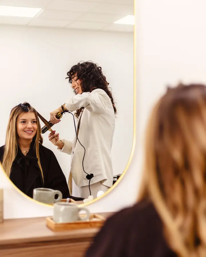 Dans le miroir, Jessica Afonso boucle les cheveux d'une cliente souriante